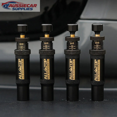 Four black tire pressure gauges with gold branding on a blurred background