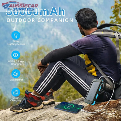 Person sitting outdoors with a 50000mAh power bank, solar panel, and USB device.